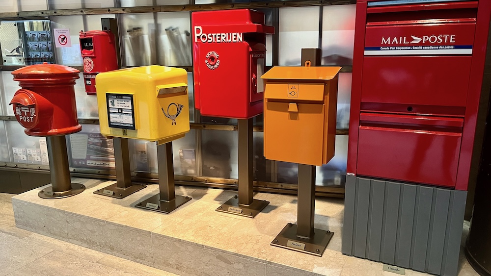 a collection of mailboxes around the world shows multiple sizes, shapes and bright colors.