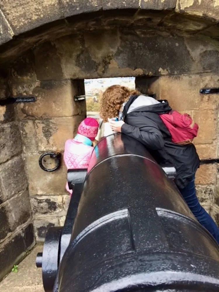 a mom and daughter peak at the view from a canon window in edinburgh castle.