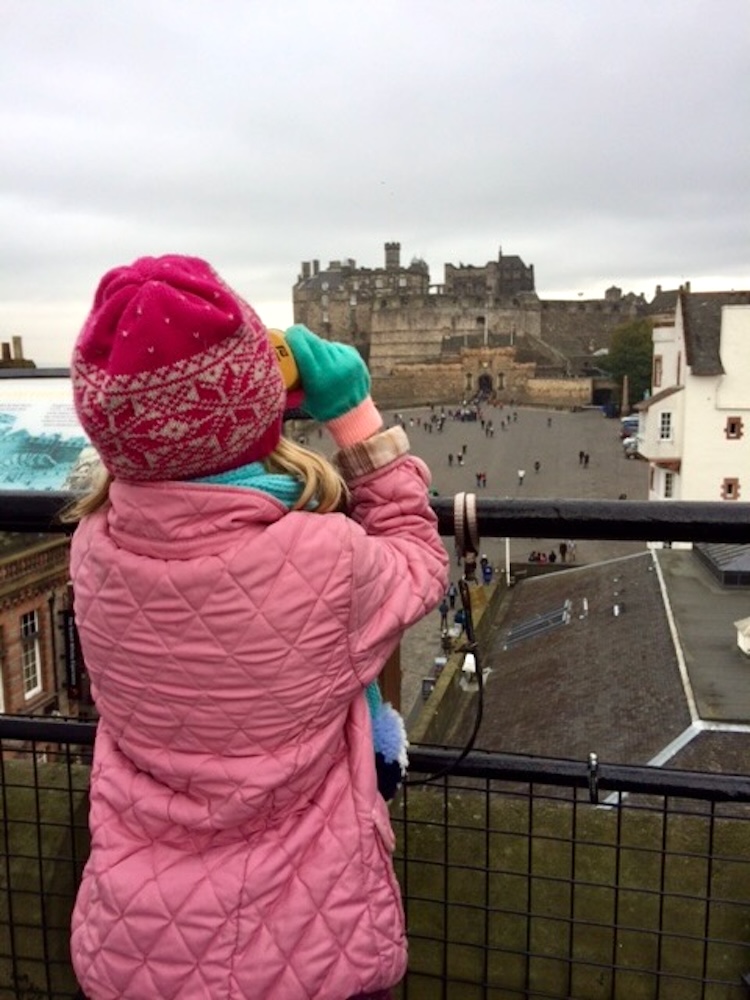 a girl looks across the courtyard of edinburgh castle through a viewfinder.