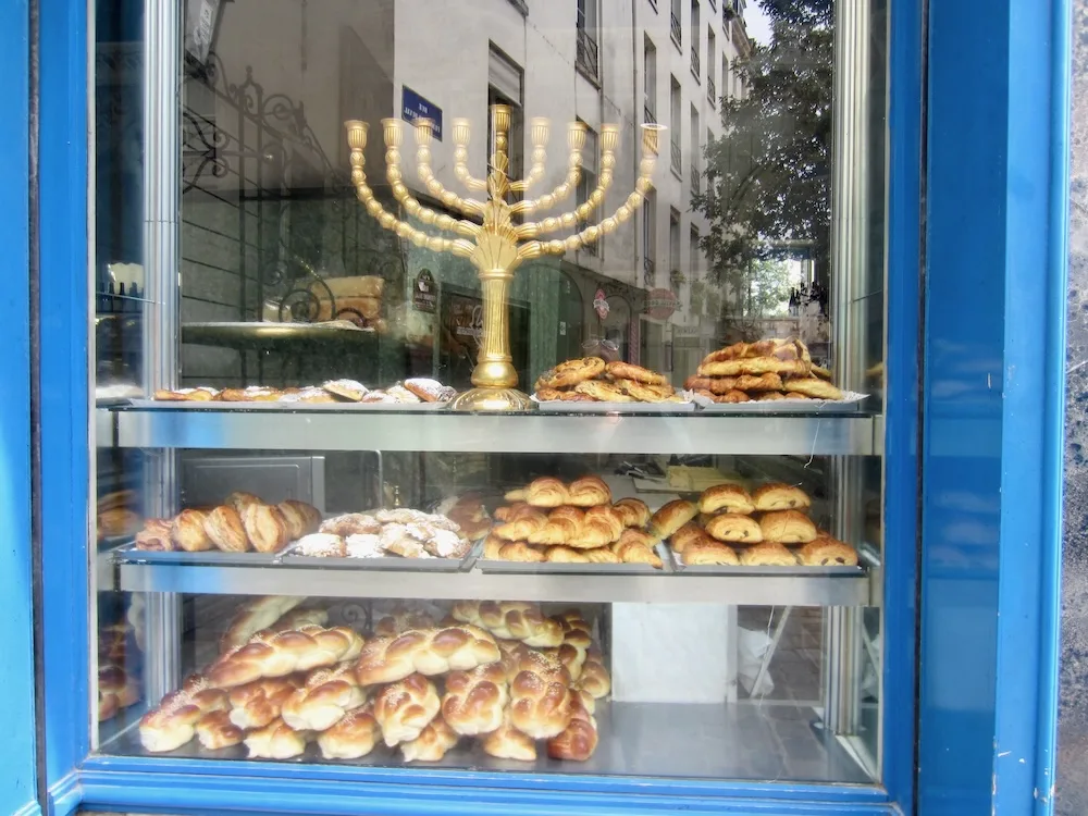 a bakery in paris' jewish quarter has a menorah and several kinds of bread in its window. the neighborhood is a cheap and fun place to eat with kids.