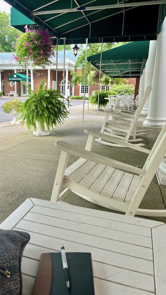 the front porch of the gideon putnam hotel has rocking chairs that invite you to relax.